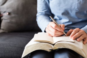 A person writing in a journal or planner, capturing thoughts or plans, with a cozy background.