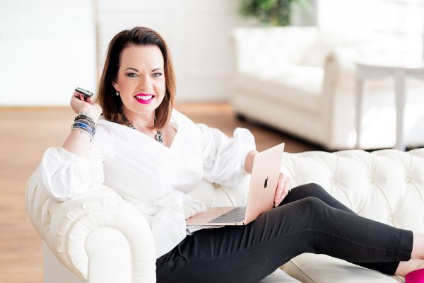 Successful woman entrepreneur working from home, using a laptop and credit card, smiling confidently in a bright, modern living room.