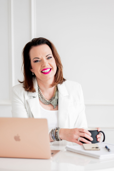 Empowered woman speaker Marie Monville with a bright smile, sitting at a desk with a laptop and coffee, promoting resilience, faith, and overcoming adversity.