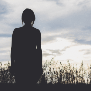 Silent reflection at sunset, silhouette of a woman standing in nature, representing hope and resilience, inspired by Marie Monville's story of overcoming adversity.