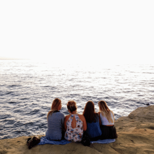 Hopeful women sitting on a cliff overlooking the ocean at sunset, symbolizing reflection, friendship, and hope.