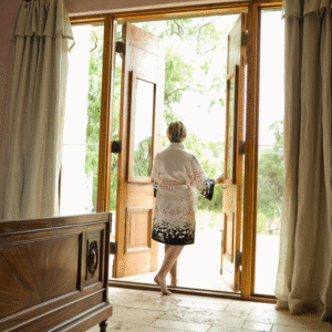 Light-filled room with wooden doorway, woman in floral kimono stepping outside, natural sunlight, serene atmosphere, Marie Monville's lifestyle photography, spiritual mindfulness, peaceful home setting.