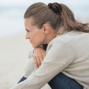 Soft-focus portrait of Marie Monville, thinking woman sitting outdoors, peaceful and reflective mood, natural background, emotional resilience, mental health awareness, inspirational speaker, contemporary lifestyle image.