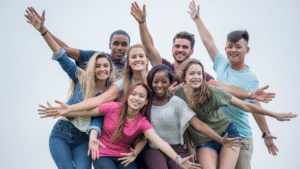Happy diverse group of young adults celebrating and smiling together, showing joy and friendship, outdoors against a bright sky background, emphasizing community and positivity for SEO.